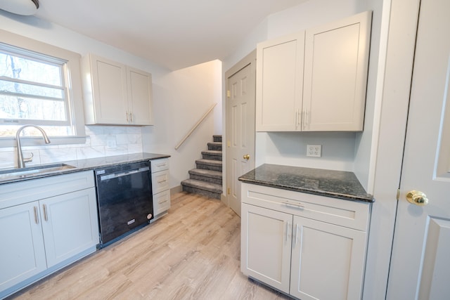 kitchen with dishwasher, dark stone counters, sink, white cabinetry, and light hardwood / wood-style floors