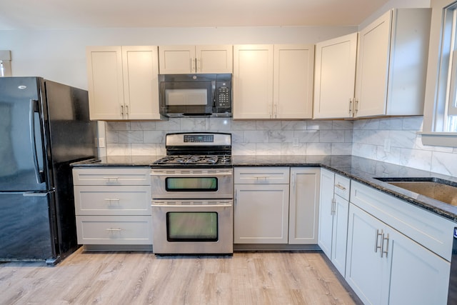 kitchen featuring tasteful backsplash, white cabinetry, dark stone counters, black appliances, and light hardwood / wood-style floors