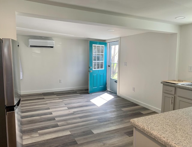 kitchen featuring stainless steel fridge, an AC wall unit, and wood-type flooring