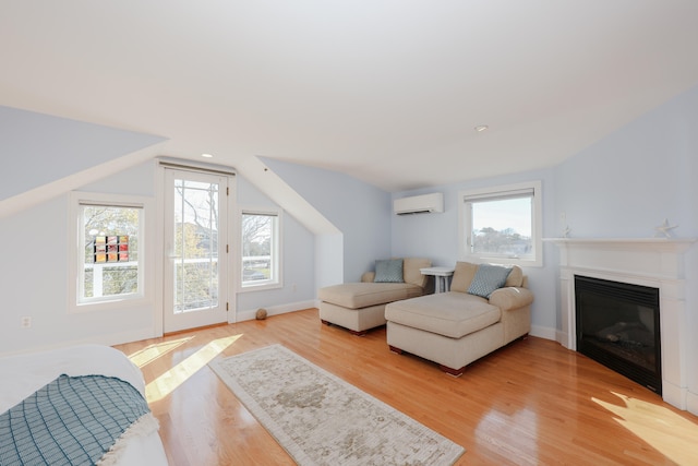 living room featuring vaulted ceiling, a wall unit AC, light wood-type flooring, and plenty of natural light