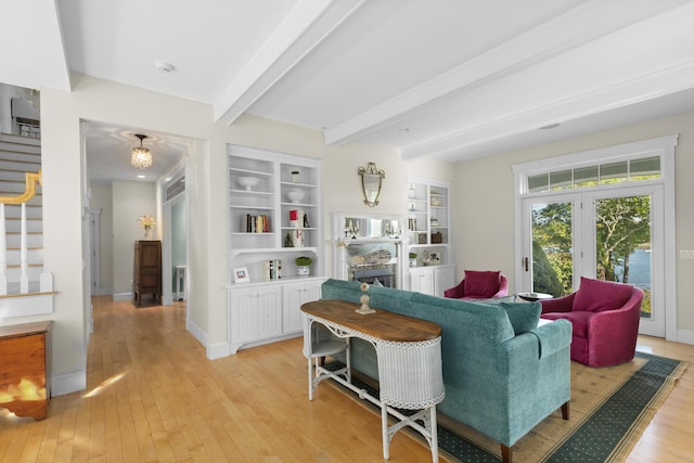 living room with french doors, a stone fireplace, built in features, beamed ceiling, and light hardwood / wood-style floors