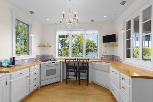 kitchen with a wealth of natural light, white range with gas cooktop, sink, decorative light fixtures, and white cabinets