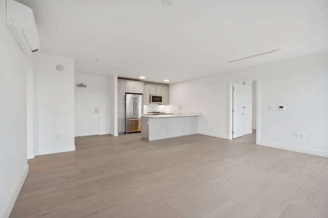 unfurnished living room featuring an AC wall unit, sink, and light wood-type flooring