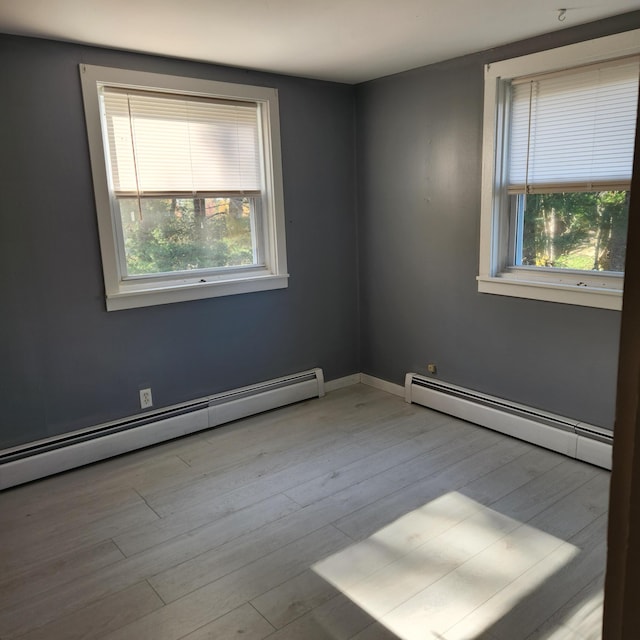 unfurnished room with light hardwood / wood-style floors, a baseboard radiator, and a wealth of natural light