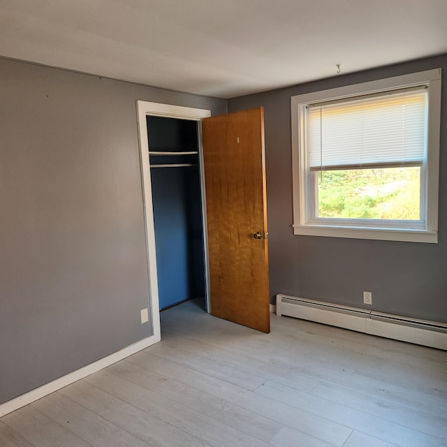 unfurnished bedroom featuring a closet, a baseboard radiator, and light wood-type flooring