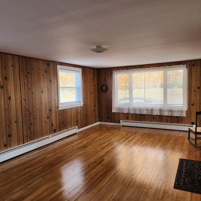 empty room with a baseboard heating unit, hardwood / wood-style flooring, and wooden walls