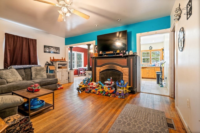 living room featuring decorative columns, wood-type flooring, ceiling fan, and a fireplace