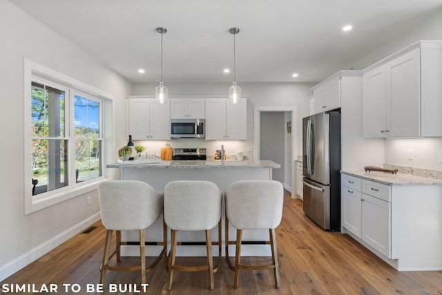 kitchen with appliances with stainless steel finishes, white cabinetry, light stone countertops, light wood-type flooring, and decorative light fixtures