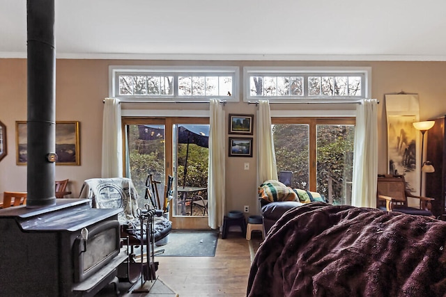 bedroom with a wood stove, access to outside, light wood-type flooring, and crown molding