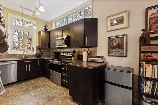 kitchen with appliances with stainless steel finishes, hanging light fixtures, a healthy amount of sunlight, and backsplash