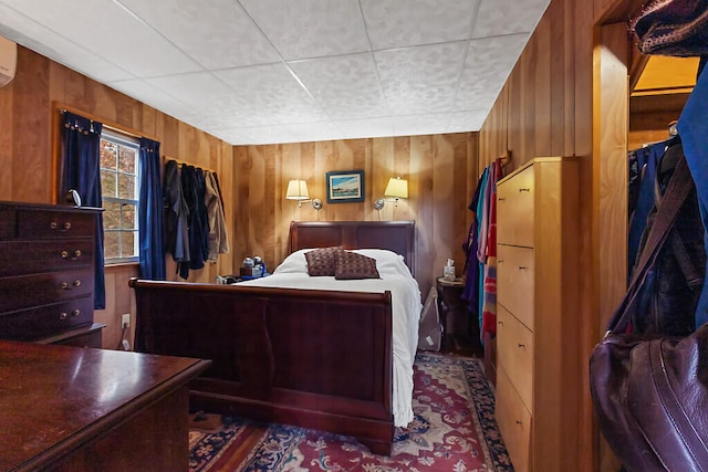 bedroom with a wall mounted AC, wooden walls, and a paneled ceiling