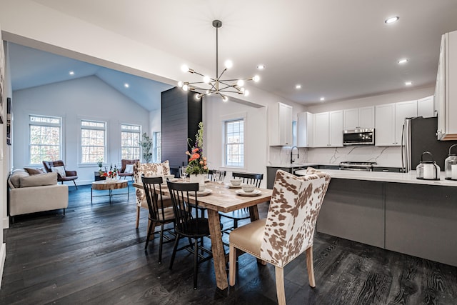 dining area featuring dark wood-type flooring, a notable chandelier, vaulted ceiling, and sink