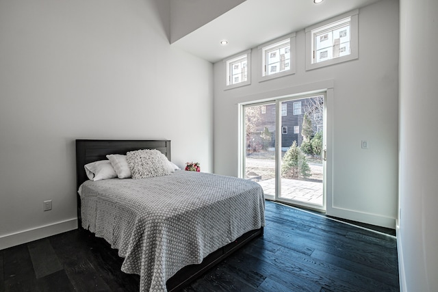 bedroom featuring access to exterior, multiple windows, a towering ceiling, and dark hardwood / wood-style flooring