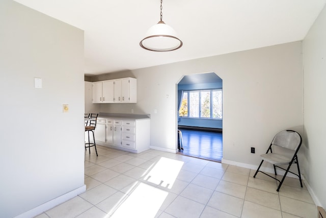 kitchen with white cabinets, decorative light fixtures, a baseboard heating unit, and light tile patterned floors