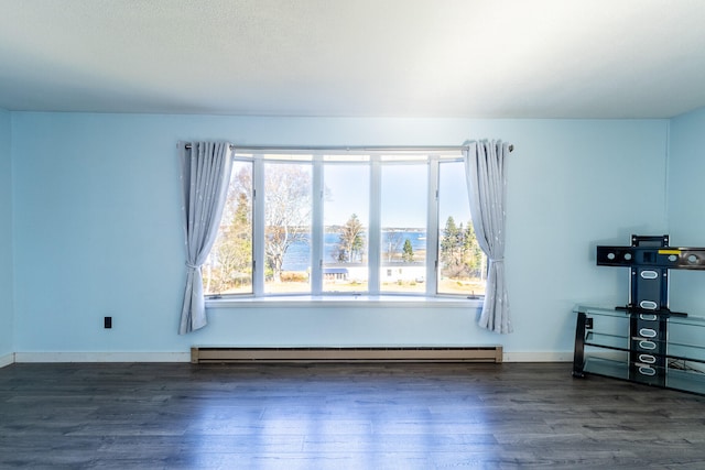 spare room featuring a baseboard heating unit, plenty of natural light, and dark hardwood / wood-style flooring