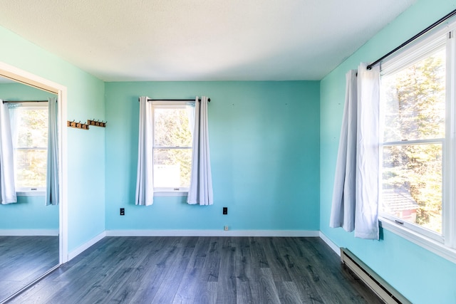 unfurnished room with a baseboard heating unit and dark hardwood / wood-style floors