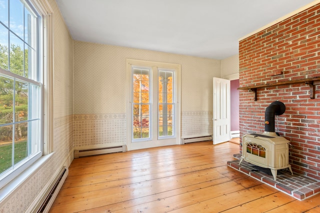 unfurnished living room featuring baseboard heating, a wood stove, and light wood-type flooring