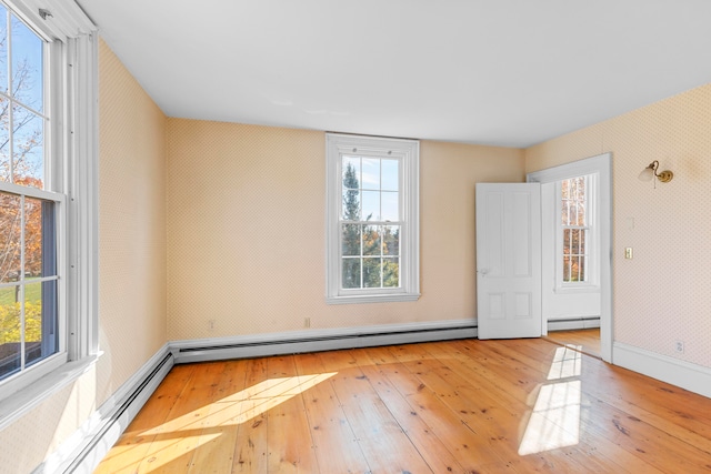 empty room with hardwood / wood-style floors, a baseboard heating unit, and plenty of natural light