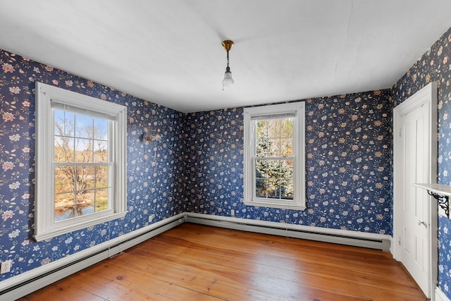 spare room with a baseboard heating unit, plenty of natural light, and hardwood / wood-style floors