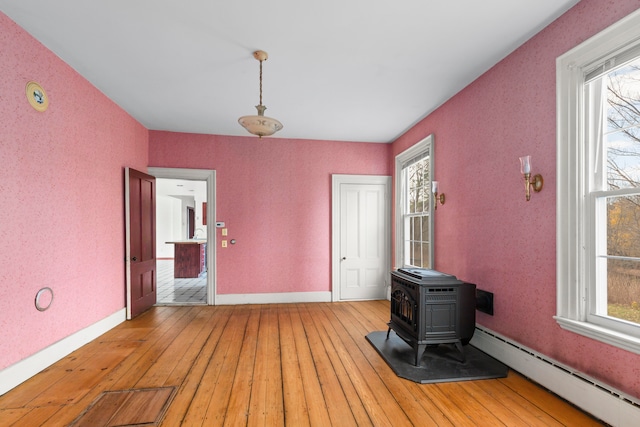 interior space featuring a wood stove, a baseboard heating unit, wood-type flooring, and plenty of natural light