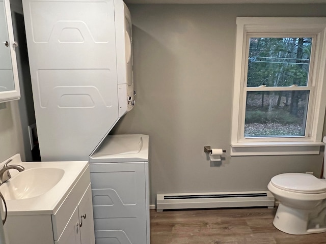 bathroom featuring a baseboard radiator, hardwood / wood-style floors, toilet, stacked washer and dryer, and vanity