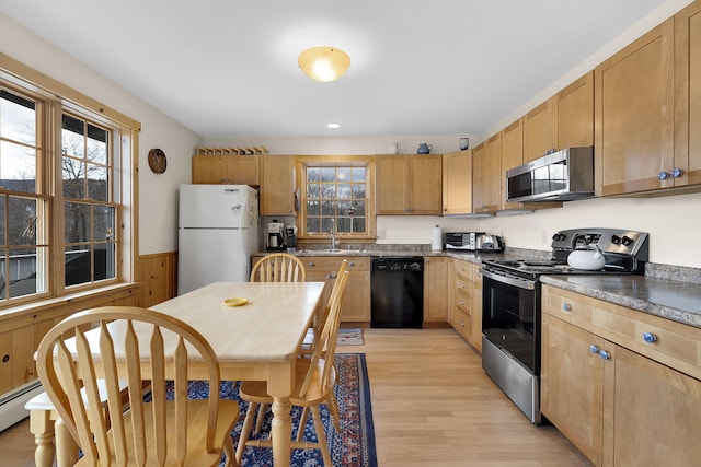 kitchen with stainless steel appliances, light wood finished floors, wainscoting, a baseboard heating unit, and a sink