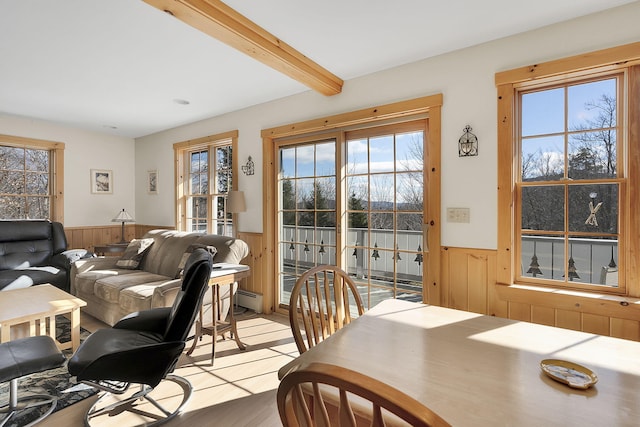 dining space with wood walls, beamed ceiling, a baseboard radiator, and light hardwood / wood-style floors