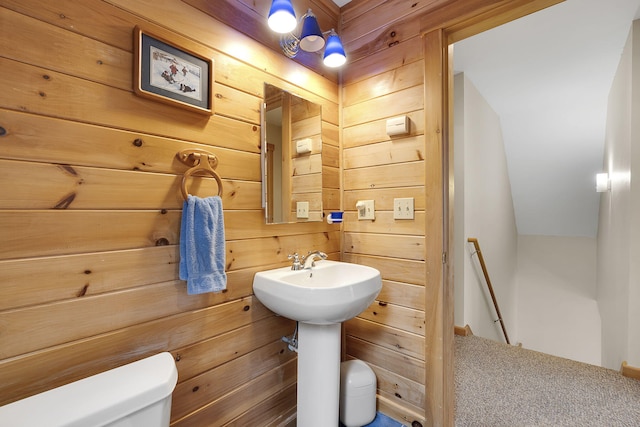 bathroom featuring toilet, sink, and wooden walls