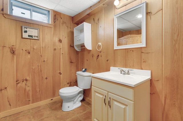 bathroom with a drop ceiling, vanity, tile patterned flooring, toilet, and wood walls