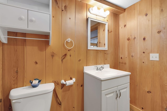 bathroom with vanity, toilet, and wood walls