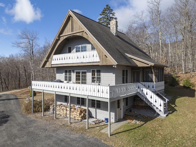 back of property featuring a shingled roof, a chimney, a sunroom, stairs, and a balcony