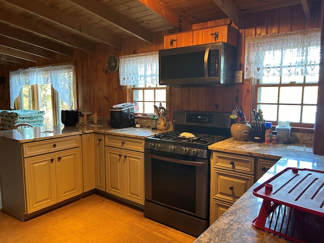 kitchen with a wealth of natural light, beamed ceiling, black gas stove, and wooden walls