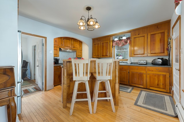 kitchen featuring a kitchen bar, light wood-type flooring, a kitchen island, hanging light fixtures, and a notable chandelier