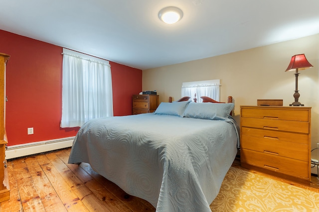 bedroom with light hardwood / wood-style floors, multiple windows, and a baseboard heating unit