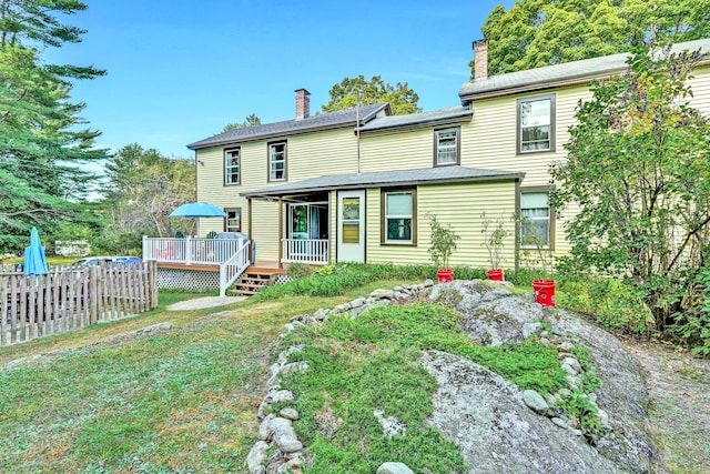 back of house featuring a wooden deck, a chimney, and fence