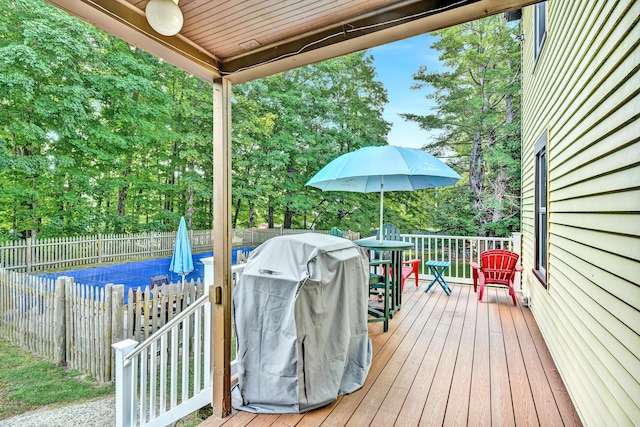 wooden deck featuring a fenced backyard, outdoor dining area, view of scattered trees, and a grill