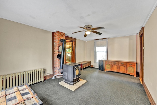 game room featuring radiator heating unit, ceiling fan, a wood stove, and baseboards