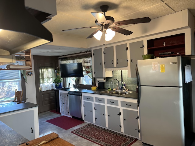 kitchen with stainless steel appliances, a sink, dark countertops, a ceiling fan, and decorative backsplash