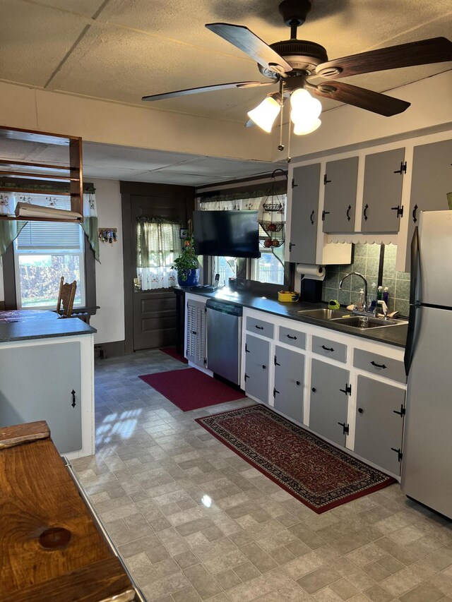 kitchen with stainless steel appliances, a sink, dark countertops, light flooring, and ceiling fan