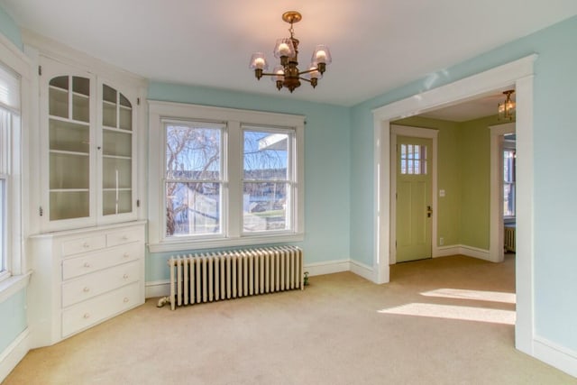 unfurnished dining area with radiator heating unit, a chandelier, and light colored carpet