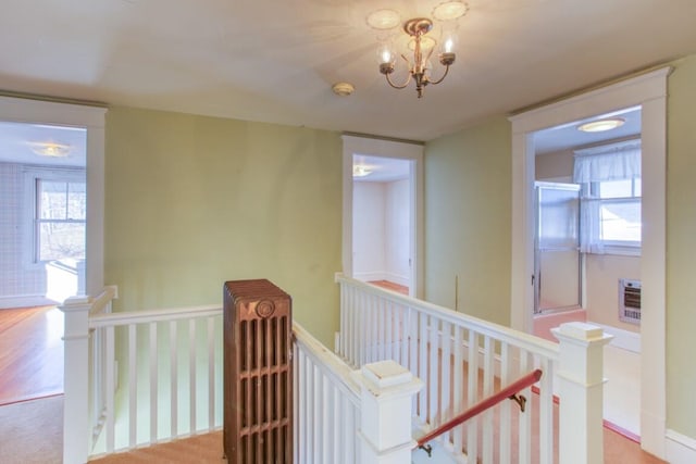 hallway with heating unit, an inviting chandelier, and light colored carpet