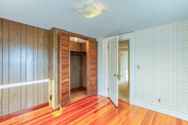 unfurnished bedroom with wooden walls, wood-type flooring, and a closet