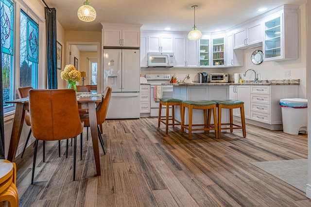 kitchen with wood-type flooring, light stone countertops, pendant lighting, white cabinetry, and white appliances