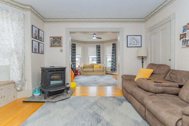 living room with ceiling fan, a wood stove, wood-type flooring, and ornamental molding