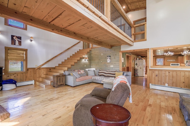 living room featuring light hardwood / wood-style flooring, a baseboard heating unit, wood walls, and a high ceiling