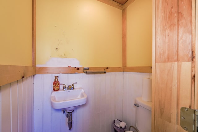 bathroom featuring sink, wooden walls, and toilet