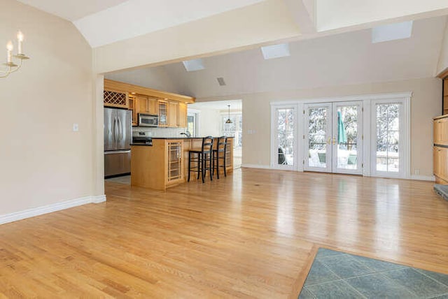 unfurnished living room with french doors, vaulted ceiling, an inviting chandelier, and light hardwood / wood-style flooring