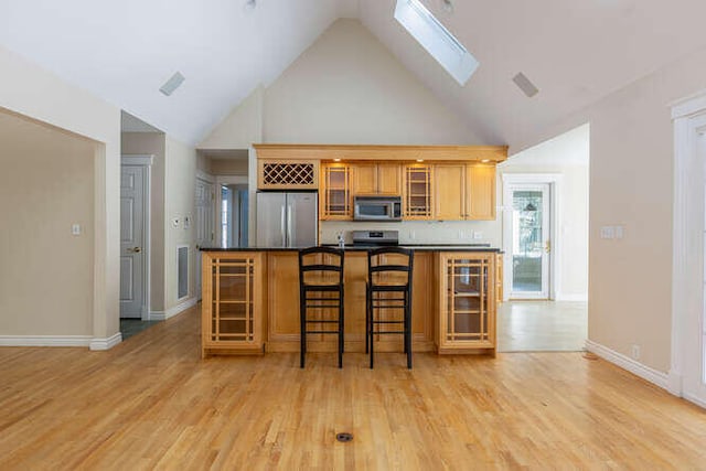 kitchen with appliances with stainless steel finishes, a breakfast bar, light hardwood / wood-style floors, and a skylight