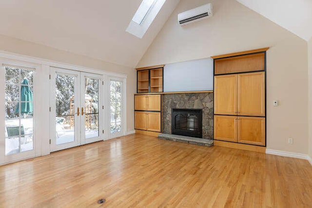 unfurnished living room with high vaulted ceiling, a wall mounted AC, a stone fireplace, french doors, and light wood-type flooring