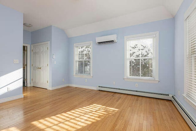 spare room featuring a wall mounted air conditioner, vaulted ceiling, light hardwood / wood-style flooring, and a baseboard heating unit